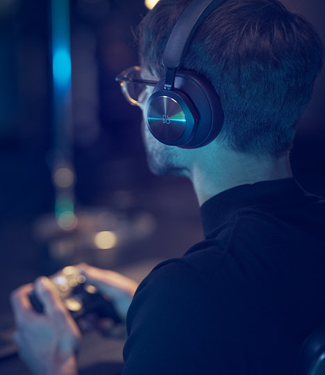 一个佩戴着 Bang and Olufsen 头戴式耳机的人坐着玩 Xbox Series X。