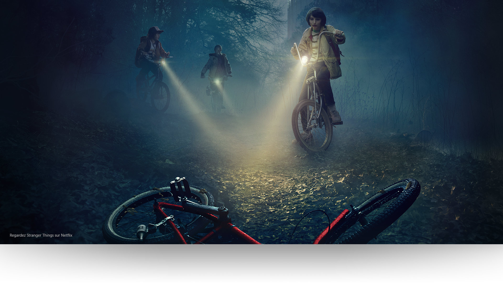 Stranger Things - Dustin, Lucas et Mike éclairent un vélo abandonné sur un sentier forestier lugubre. Regardez Stranger Things sur Netflix.