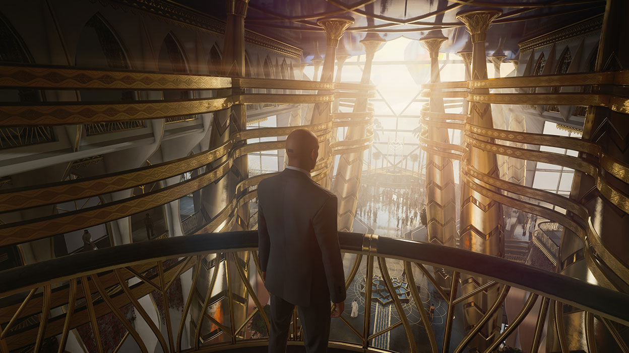 Agent 47 stands on a balcony in a building with a gathering of people below
